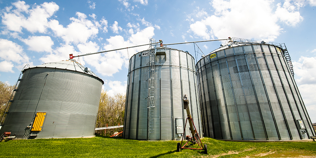 View of three grain bins against blue sky and puffy clouds