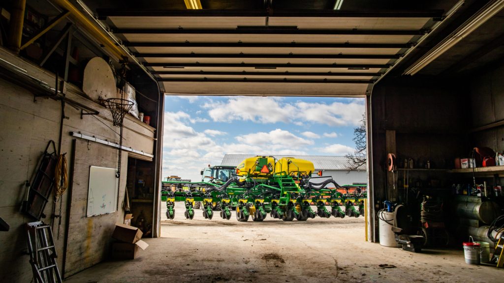 Looking out from a dimly lit garage at sunlit farm equipment ready for planting season 