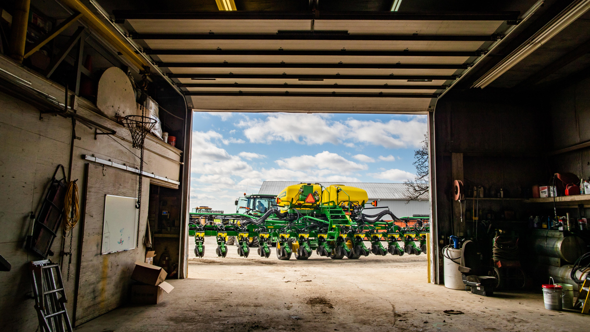 Looking out from a dimly lit garage at sunlit farm equipment ready for planting season