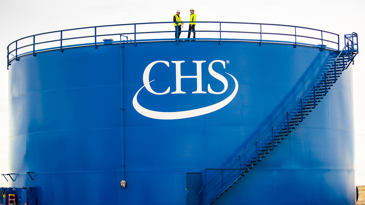 Two people in PPE standing on top of a large blue storage bin with a CHS logo